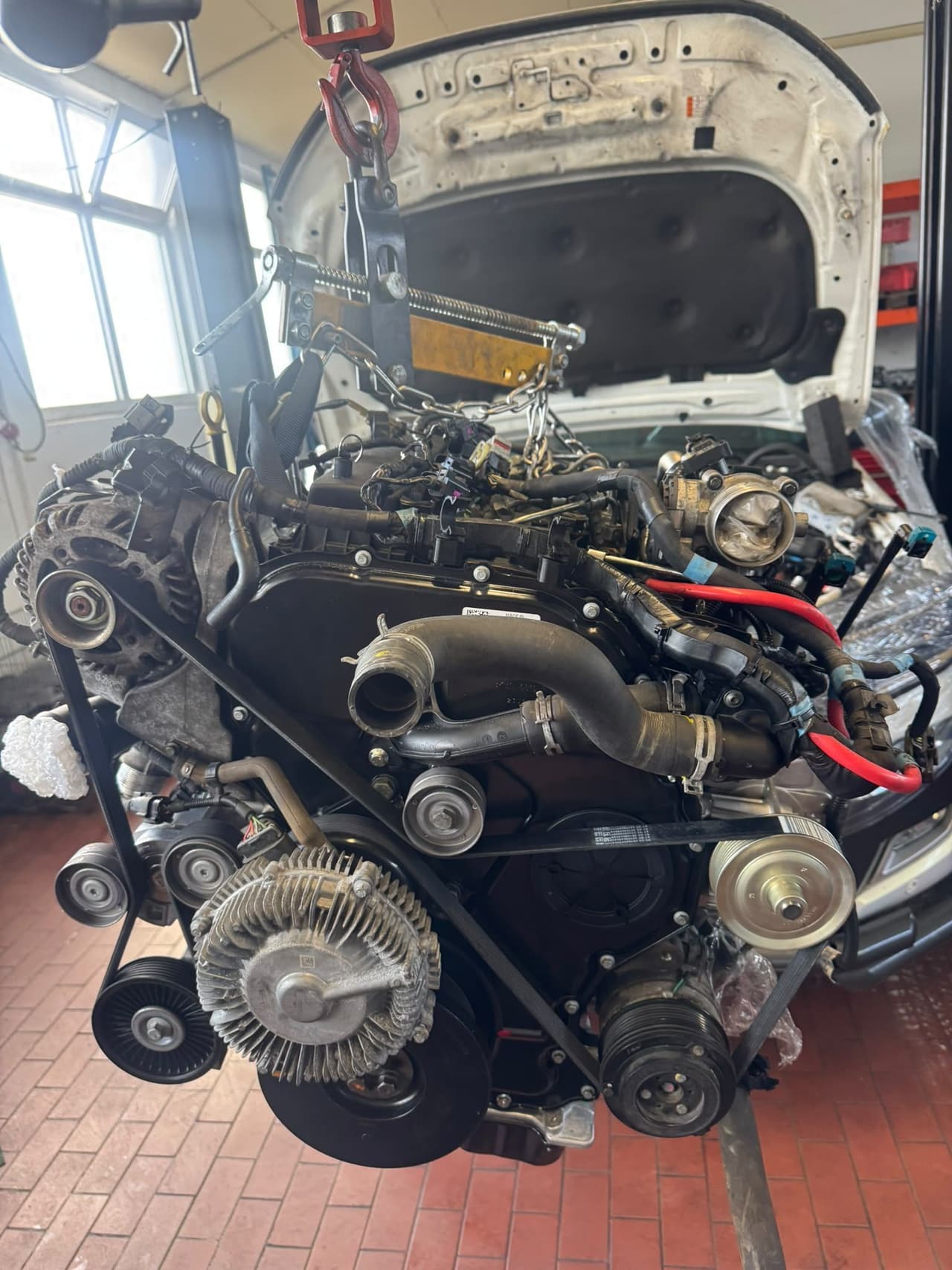 Ausgebauter Ford-Ranger-Dieselmotor am Motorkran vor dem geöffneten Fahrzeug in der Werkstatt