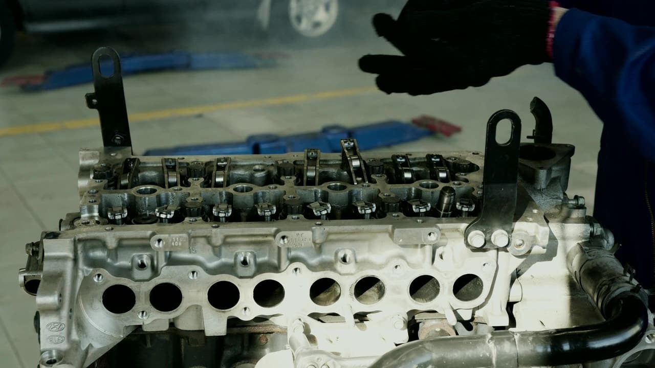 Mechaniker mit Arbeitshandschuhen am offenen Zylinderkopf eines Dieselmotors in der Werkstatt