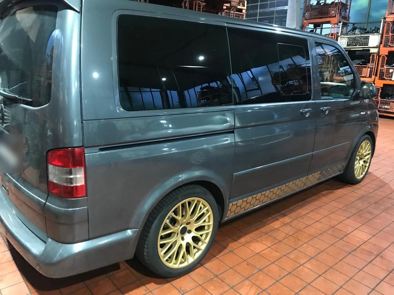 Grauer VW T5 vor dem Facelift mit goldenen Felgen, Seitenansicht in der Werkstatthalle